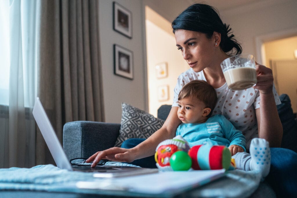Mother working on laptop holding infant